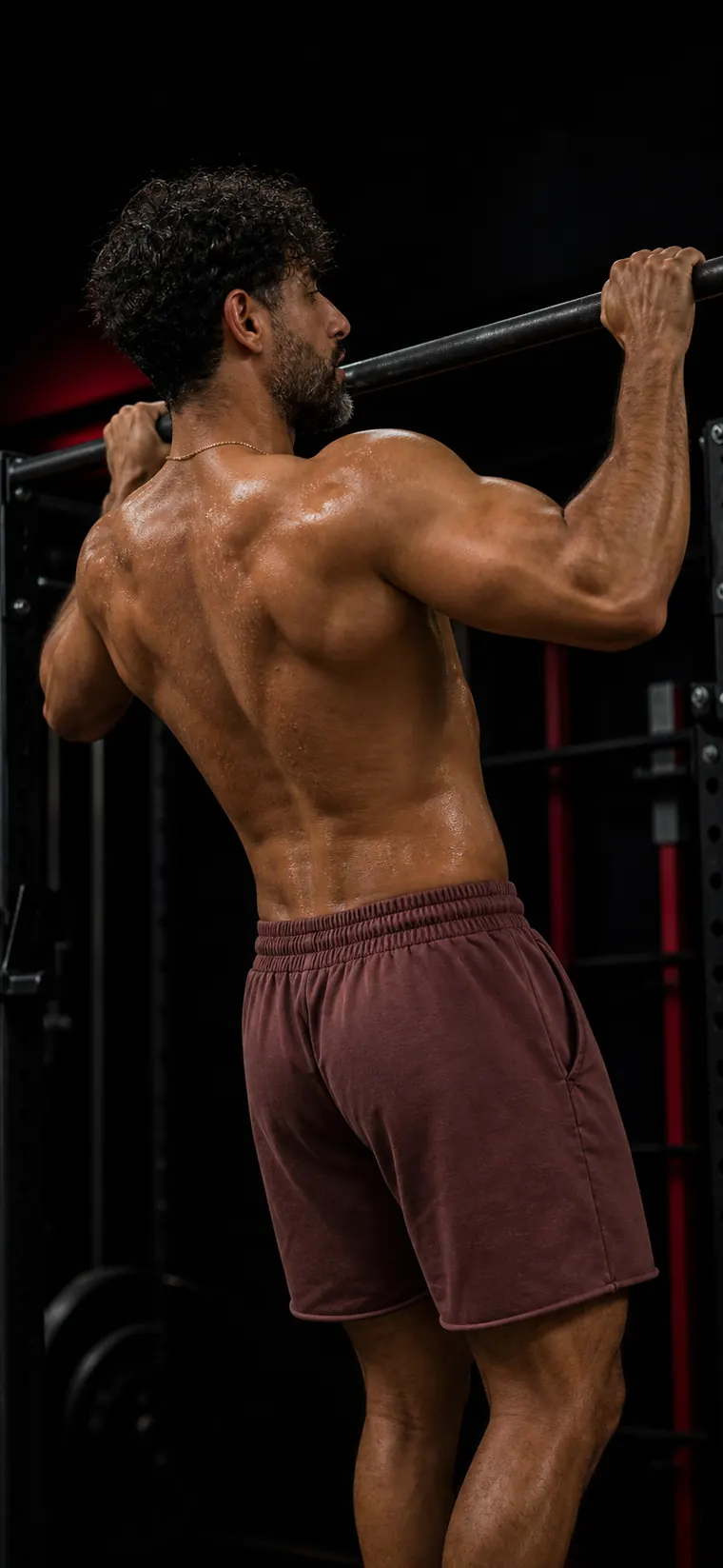 Will Frometa from behind, gripping a pull-up bar, back muscles flexed